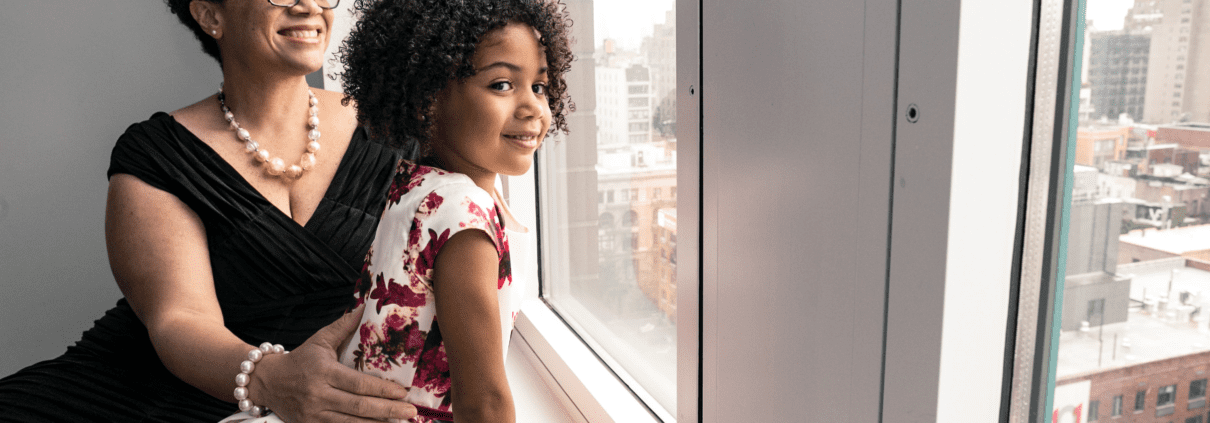 A woman holding a girl next to a window