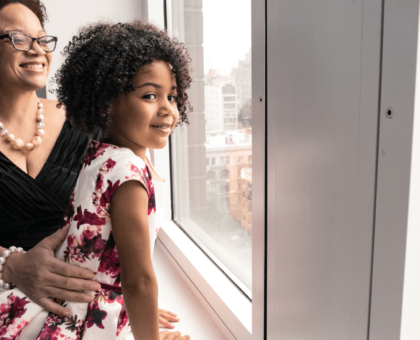 A woman holding a girl next to a window